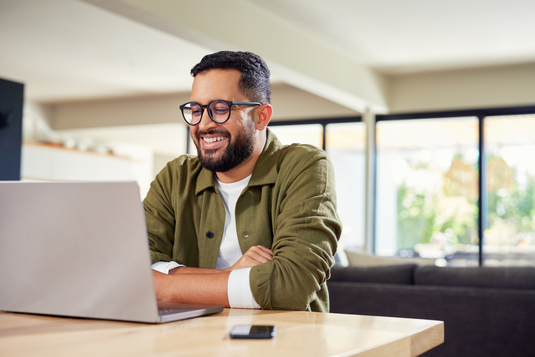 Temp Staffing Agency Dallas - Smiling young Indian man sitting at office while using laptop.