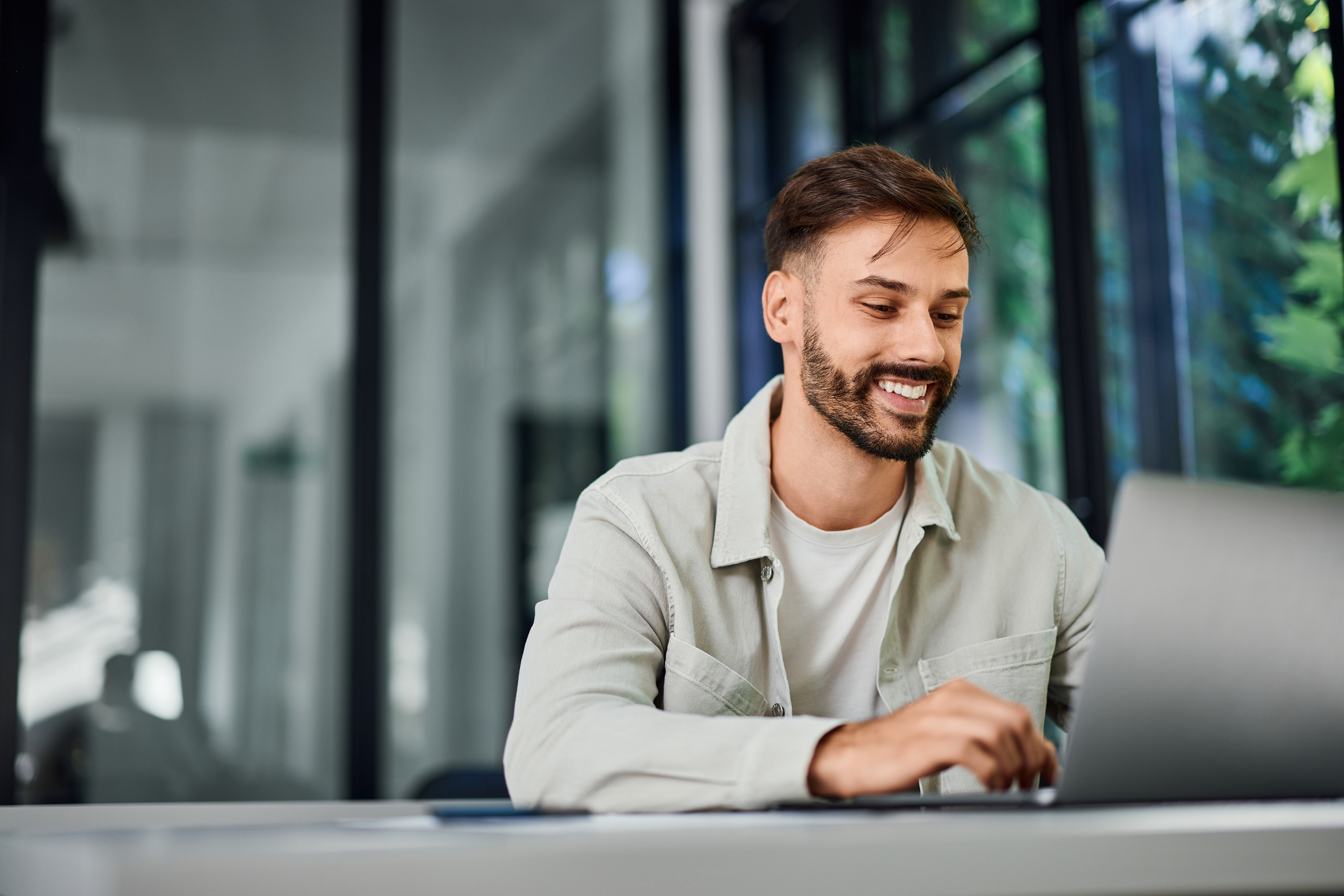 Job Search Dallas - A smiling man, working over the laptop, at the office.