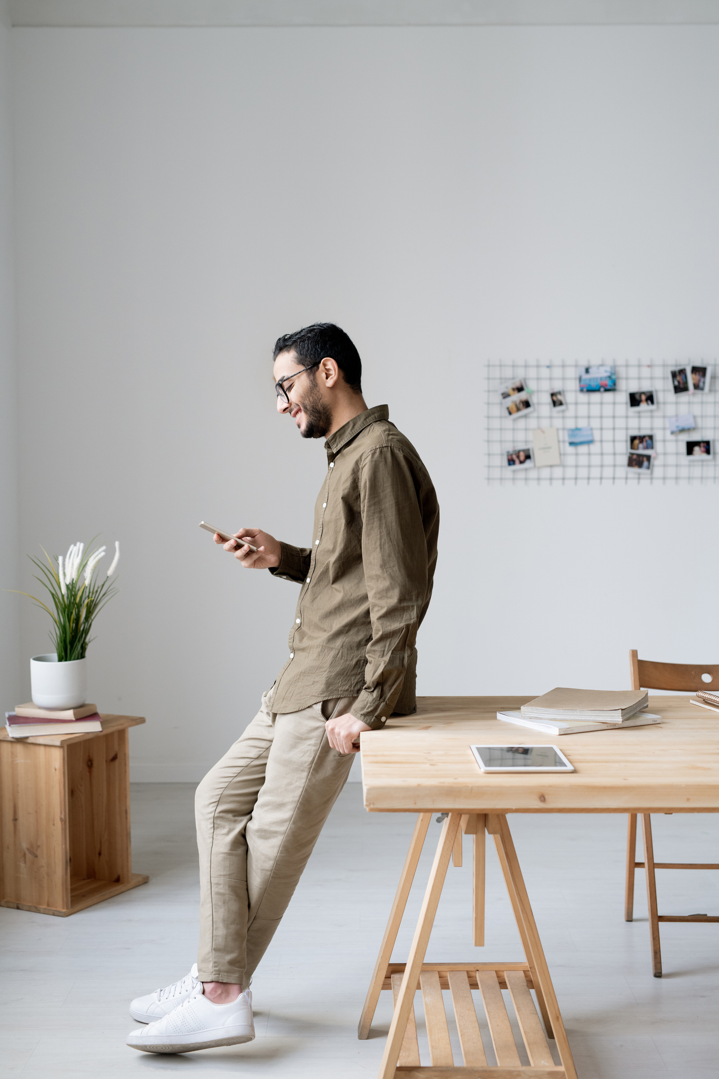 Temporary Staffing Dallas TX - Young business employee in casualwear scrolling in smartphone while standing by table in front of office window